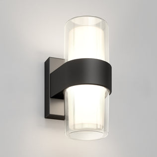 The Artika Colton modern LED indoor-outdoor wall light 5 CCT features a cylindrical frosted glass shade with a black metal band and square base, shown mounted on a light gray wall.
