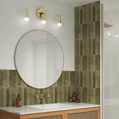 A modern bathroom features green vertical tiles, a round mirror above a wooden vanity, gold faucets, and the Artika Wayden LED mid-century bathroom vanity light (3 CCT) above the mirror. Brown bottles are arranged on the counter.