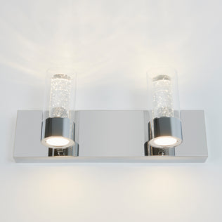 The Artika Ratio 2-light LED bathroom vanity light features a rectangular chrome base and two bubble glass shades, emitting bright white light, and is shown mounted on a white wall.