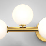 A modern wall sconce with a gold metallic fixture and three round, frosted white glass globes arranged in a triangular formation against a light gray background.