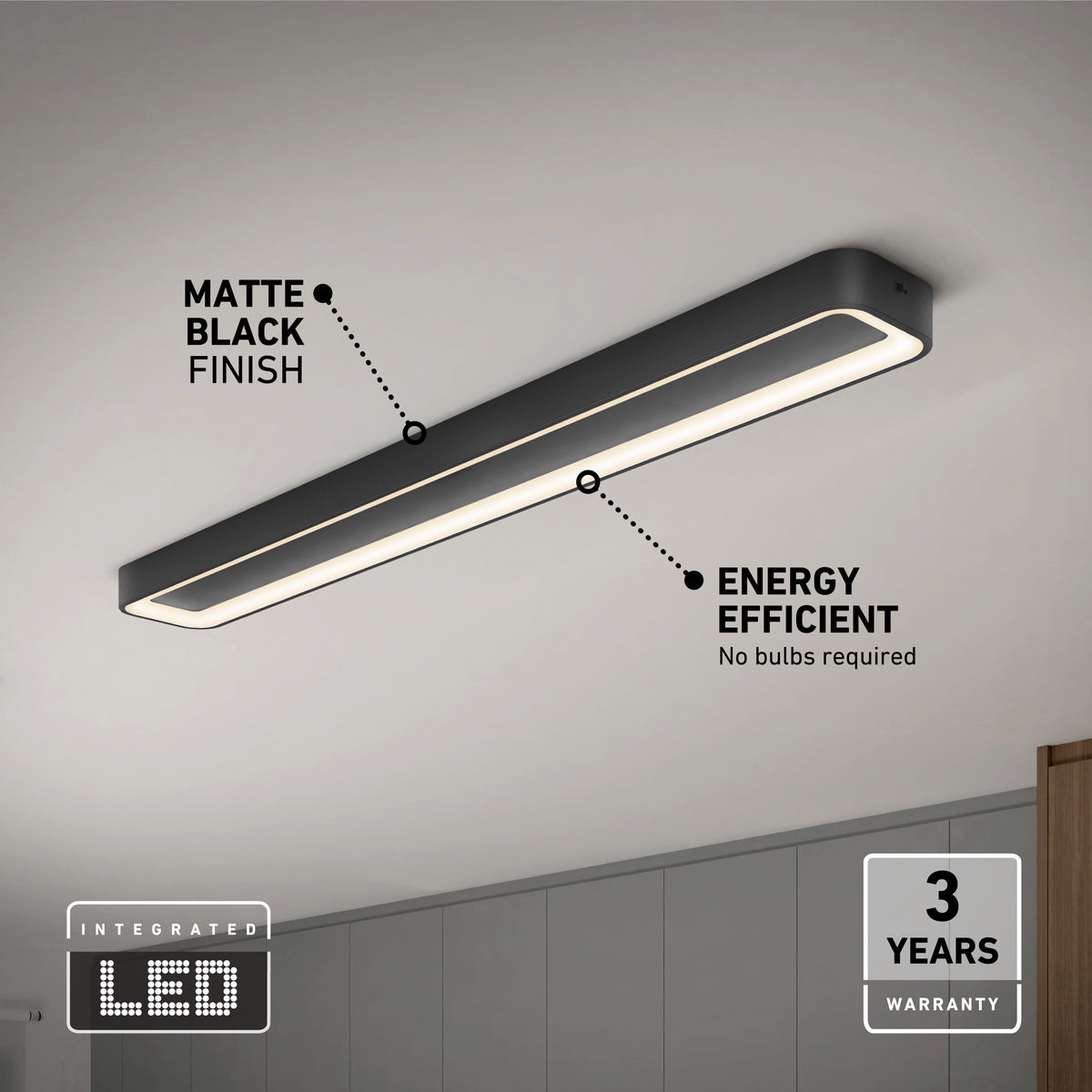 A matte black integrated LED ceiling light fixture is mounted on a white ceiling, labeled as energy efficient with no bulbs required and a 3-year warranty. The room features neutral-colored walls and cabinets.