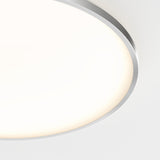 Close-up of a round, modern ceiling light with a metallic rim and a glowing white diffuser, mounted on a white ceiling. Only part of the fixture is visible in the image.