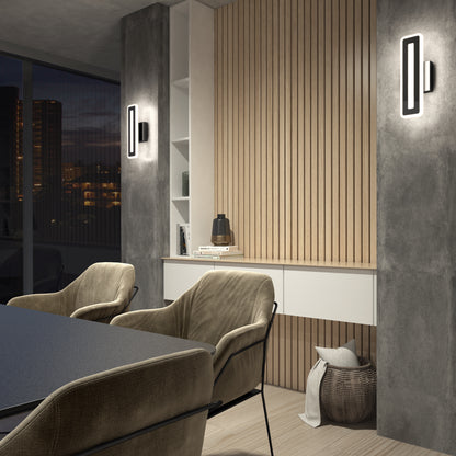 Modern office with beige armchairs, black table, wooden slat wall, built-in shelves, and two Artika Evasion modern indoor-outdoor LED wall lights (3 CCT). A basket sits beneath a drawer; large windows reveal city buildings at night.