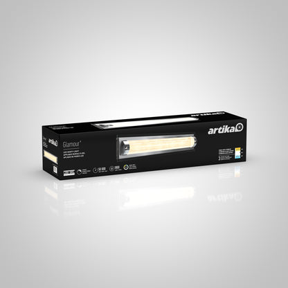 A rectangular black box for the Artika Glamour LED bathroom vanity light 3 CCT, showing the fixture image, product details, and lighting feature icons on the front, against a plain gradient gray background.