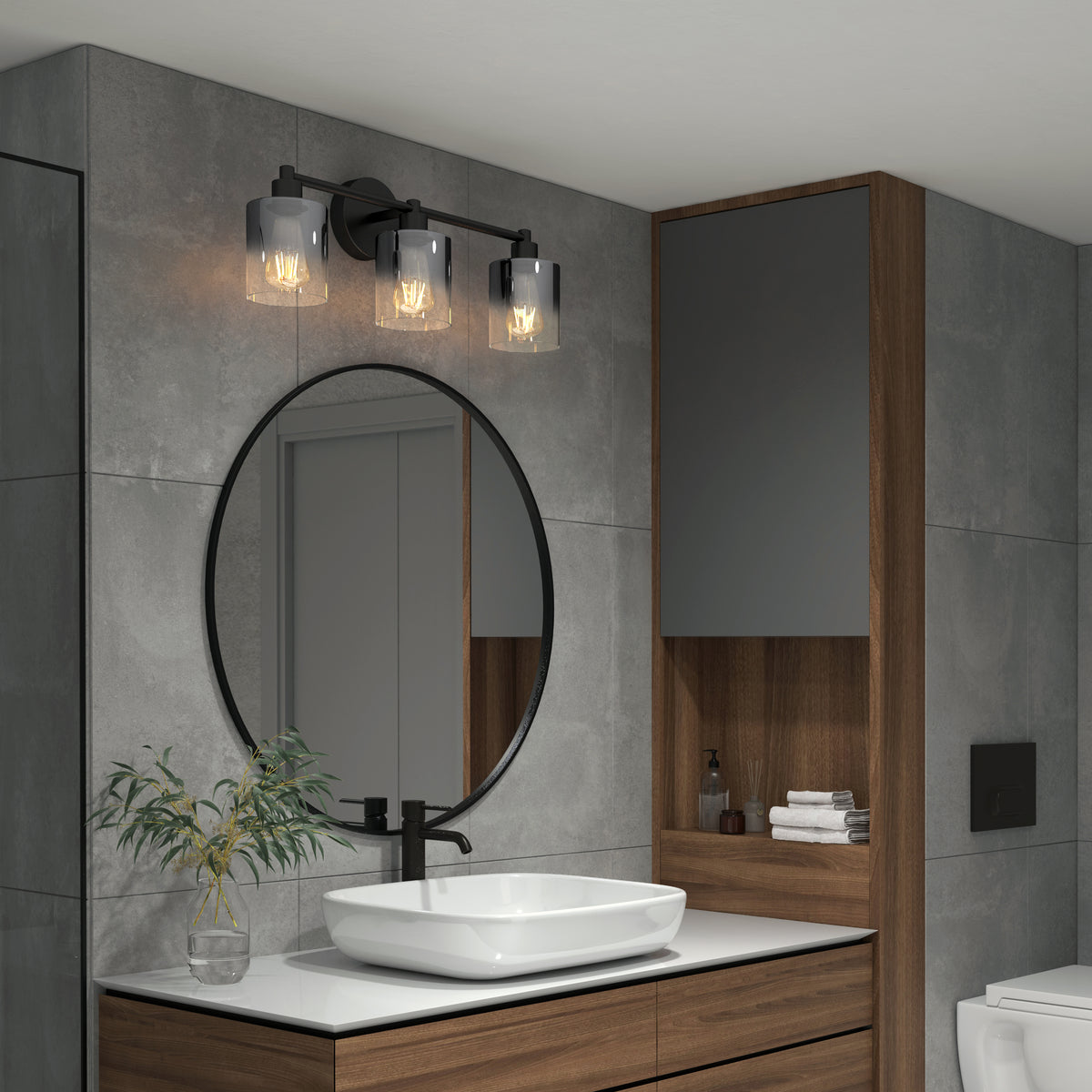Modern bathroom with gray tiles, a round black-framed mirror above a white vessel sink, wood cabinetry, and a three-bulb black wall light fixture. A small plant sits on the countertop near the sink.