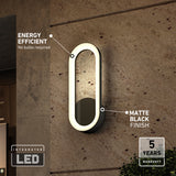 A modern oval wall light fixture with a matte black finish is mounted on a textured wall. Text highlights its energy efficiency (no bulbs required) and integrated LED, with a 5-year warranty badge in the corner.