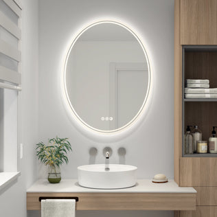 A modern bathroom features the Artika Corby 22 in. x 28 in. LED mirror with defogger above a white vessel sink on a wooden vanity, accented by a plant, soap dish, towel, and shelves with toiletries on the right.
