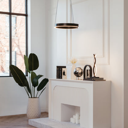 A modern living room features a white mantel adorned with books, a globe, and sculptures. Nearby stands a large potted plant, while the Artika Vance modern LED pendant light 3 CCT hangs above the mantel from the ceiling.