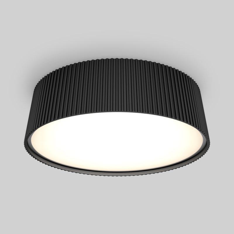 The Artika Groove 13 in. LED modern flush mount light features a black, ribbed exterior and a bright white surface, adding style to any space with its 5 CCT settings, shown installed on a light gray ceiling.