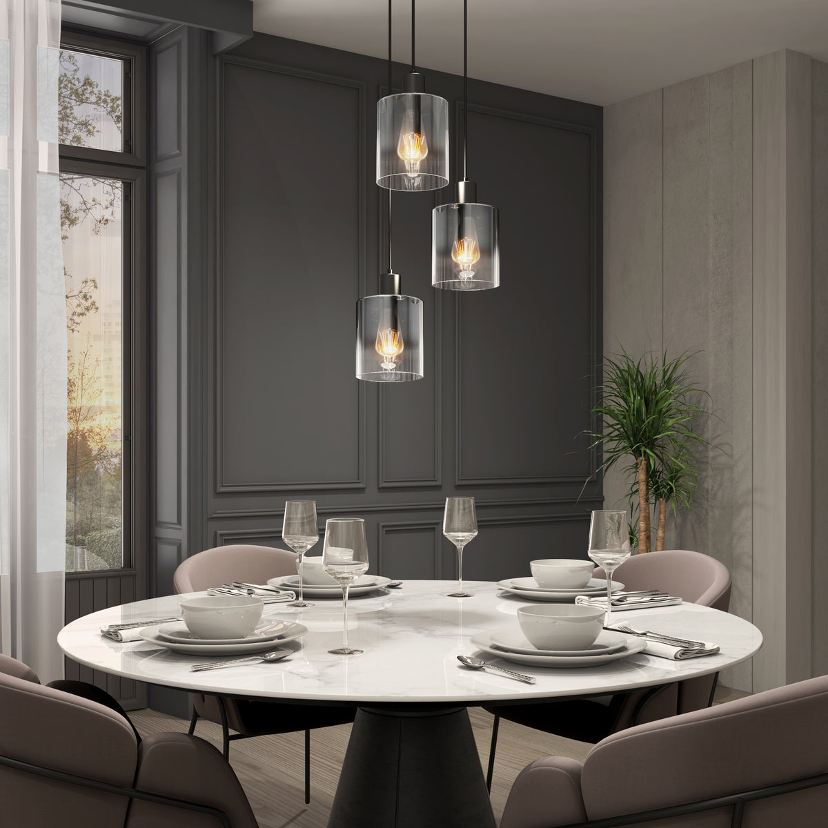 A modern dining room with a round white marble table set for four, surrounded by beige chairs. Three pendant lights hang above the table, and a tall plant stands in the corner near large windows with sheer curtains.