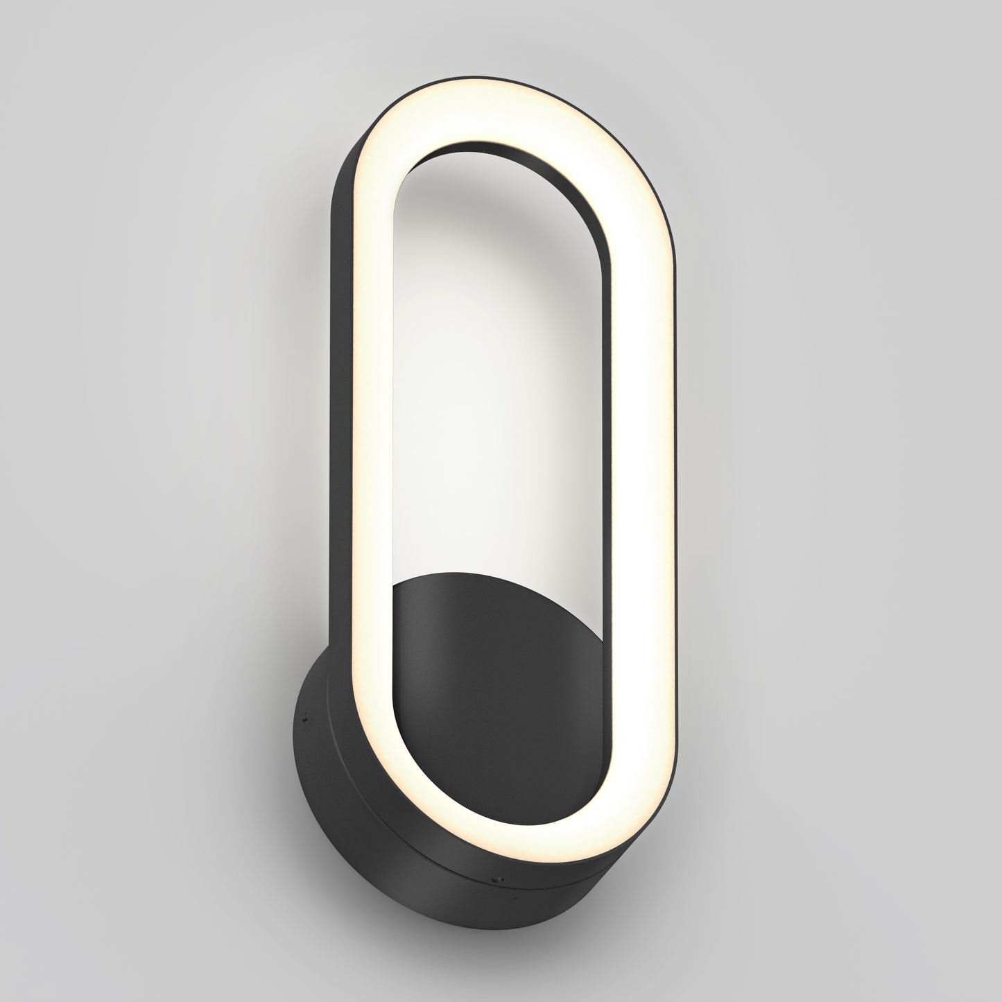 The Artika Aiden modern LED indoor-outdoor wall light 5 CCT features a black circular base and an oval LED frame, mounted vertically on a plain light gray wall.