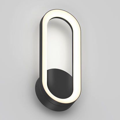 The Artika Aiden modern LED indoor-outdoor wall light 5 CCT features a black circular base and an oval LED frame, mounted vertically on a plain light gray wall.