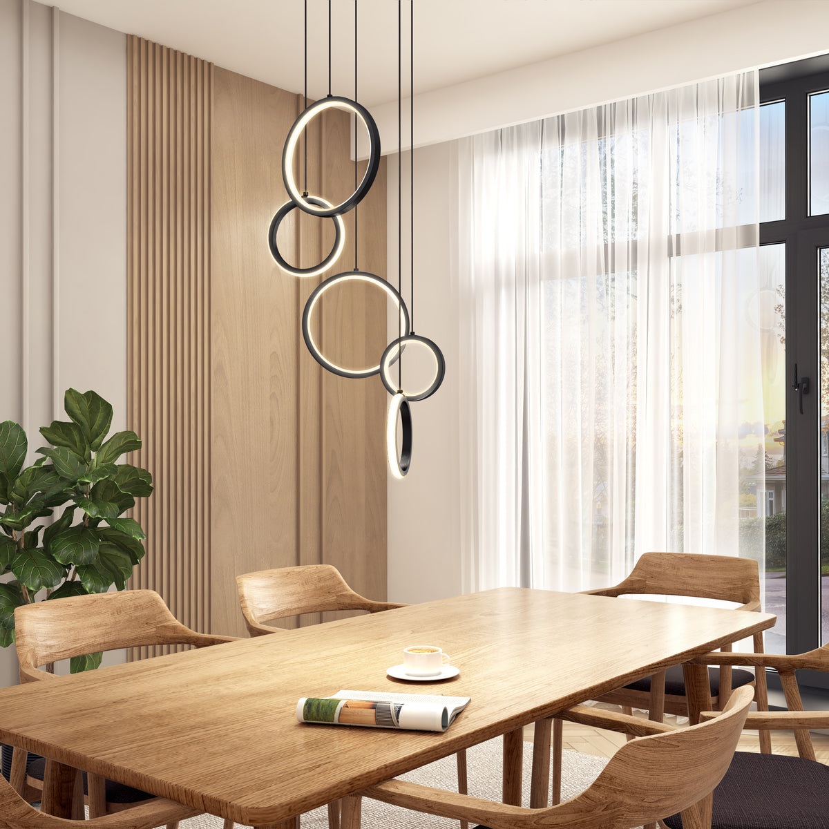 A modern dining room with a wooden table, four chairs, a potted plant, large windows with sheer curtains, and a contemporary circular pendant light fixture hanging above the table. A cup and saucer sit on the table.