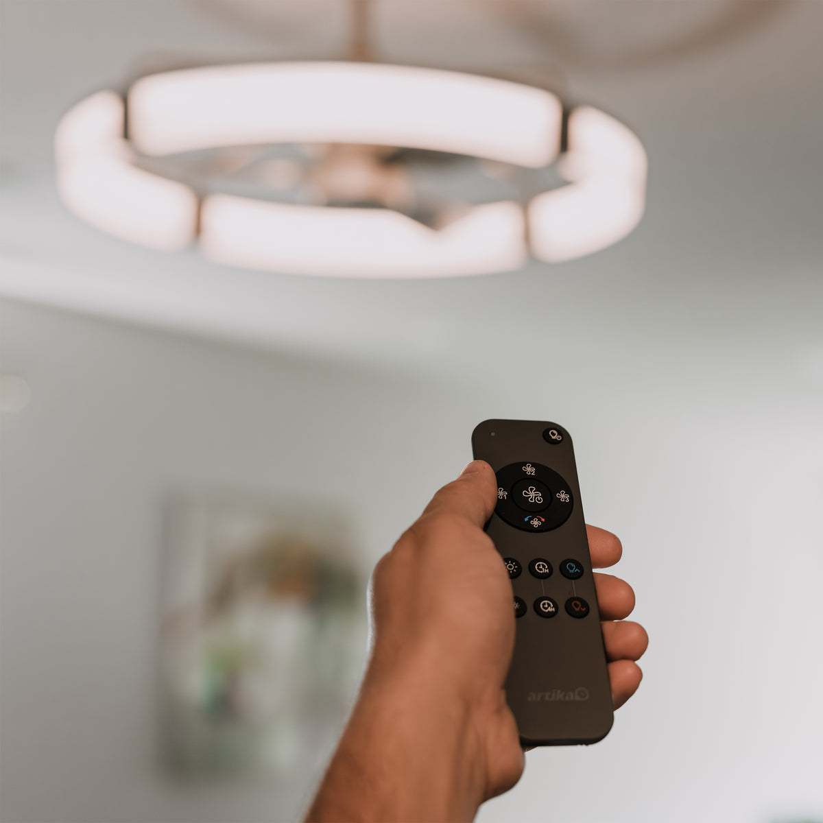 A hand holds a remote, pointed at the Artika Sunnyvale 28 in. LED modern fandelier ceiling fan with light.