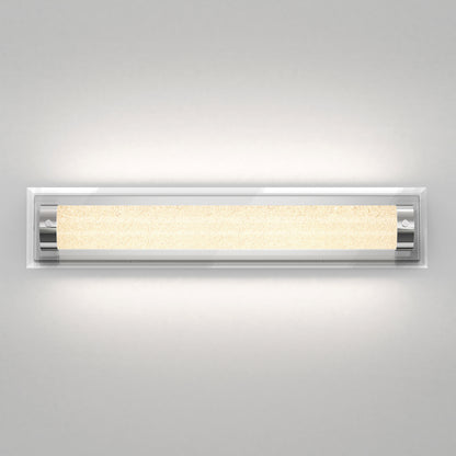 The Artika Glamour LED bathroom vanity light 3 CCT features a modern rectangular design with chrome accents and a textured illuminated central panel, casting a warm glow against a light gray wall.
