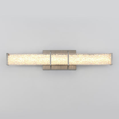 The Artika Royale LED bathroom vanity light features a rectangular, textured glass shade and a metallic base, providing a warm, even glow against a plain light gray wall.