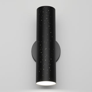 The Artika Cosmic indoor-outdoor LED wall light 3 CCT is a black cylindrical fixture with star-like perforations, mounted on a round base and emitting light from the bottom, shown against a plain white background.
