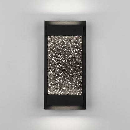 The Artika Essence Glow Box indoor-outdoor LED wall light features a modern black frame and rectangular design, casting up-and-down lighting through a textured panel filled with star-like dots for a sparkling effect on gray walls.