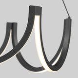 A close-up of a modern chandelier with curved black arms and integrated white LED light strips, set against a plain light gray background.