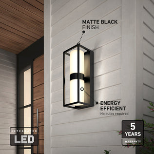 The Artika Sherman modern LED indoor-outdoor wall light 5 CCT features a matte black finish, is energy efficient with a 5-year warranty, requires no bulbs, and is shown mounted on a white wall with a small plant in the corner.