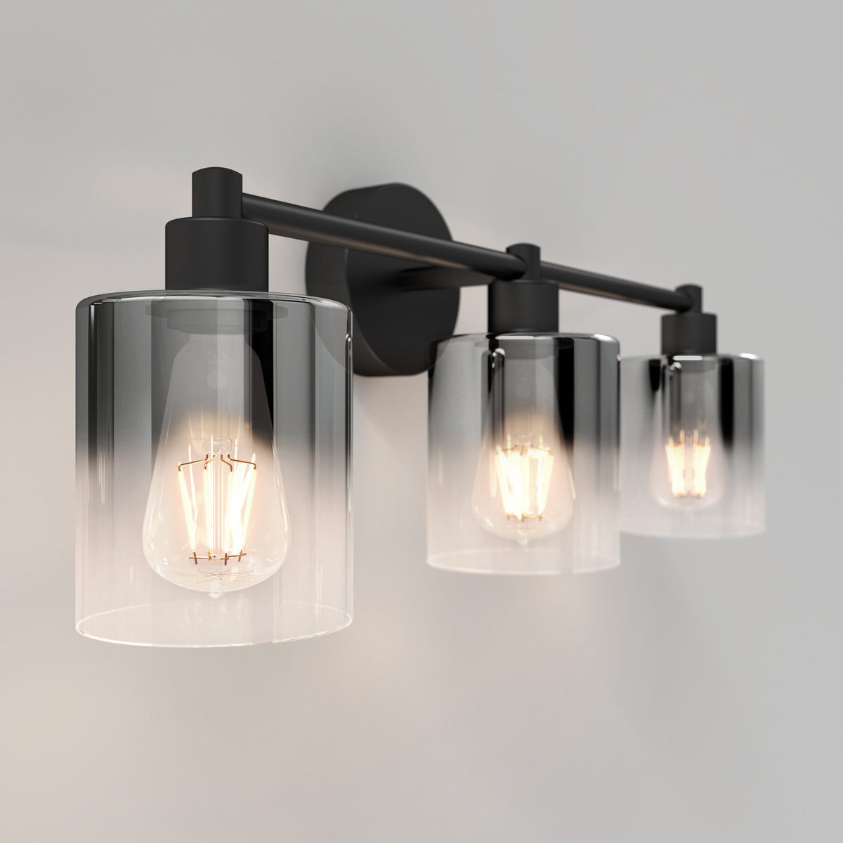The Artika Haze modern 3-light bathroom vanity light features exposed bulbs in cylindrical clear glass shades and a dark metal frame, casting a warm glow against neutral walls.