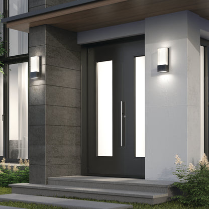 Modern front entrance with a black door featuring vertical frosted glass panels, gray stone, white walls, steps, Artika Dixon indoor-outdoor LED wall lights mounted on either side of the door, and small plants by the steps.