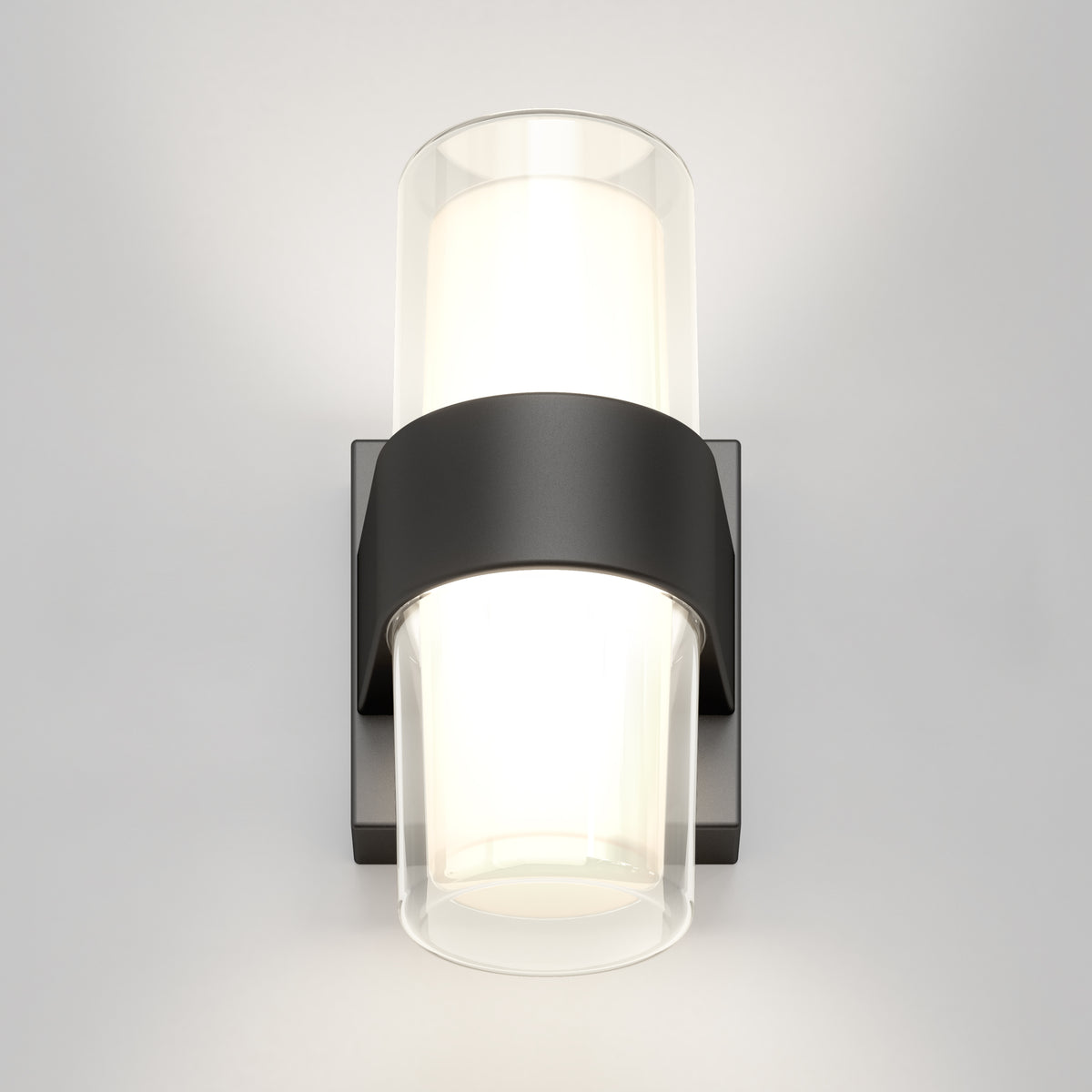 A modern wall sconce with a black rectangular base and two cylindrical glass shades, emitting soft white light, mounted on a plain light-colored wall.