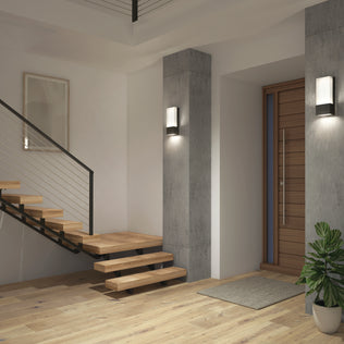 Modern entryway with floating wooden stairs, concrete pillars featuring the Artika Dixon indoor-outdoor LED wall light, a wooden front door, framed wall art, a small corner plant, and light wood flooring.