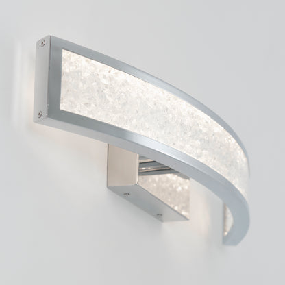 The Artika Glitter LED bathroom vanity light features a modern, wall-mounted design with a curved silver frame and textured frosted glass, emitting a soft white glow thats perfect for any space.