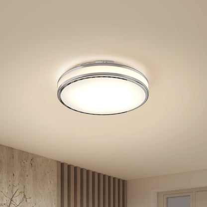 The Artika Hemisphere 15 in. LED flush mount light 5 CCT, a modern round fixture with adjustable brightness, is installed on a beige ceiling in a contemporary room featuring wood paneling and a window.