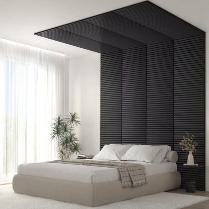 A modern bedroom features the Artika Sonolok 15.5 ft sound-absorbing wall panel kit as a textured black accent wall extending onto the ceiling, paired with a beige platform bed and large windows with sheer curtains and potted plants.