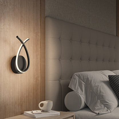 A modern bedroom features a tufted headboard, neatly made bed with gray bedding and a bolster pillow, a nightstand with book and cup, and the Artika Gamma modern LED wall sconce 5 CCT mounted on a wooden panel.
