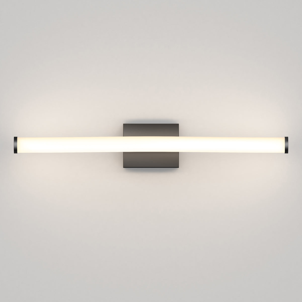 A modern wall-mounted light fixture with a long, horizontal frosted tube emitting soft white light, attached to a small rectangular metallic base.