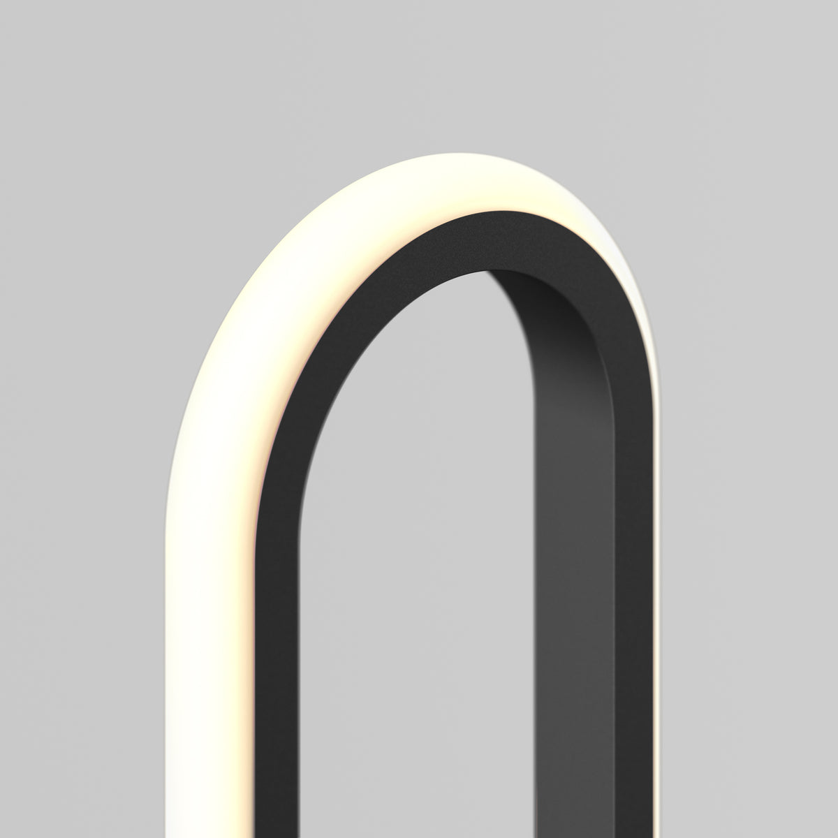 A close-up of a modern, minimalist lamp with a black frame and a glowing, curved white light on a plain gray background.