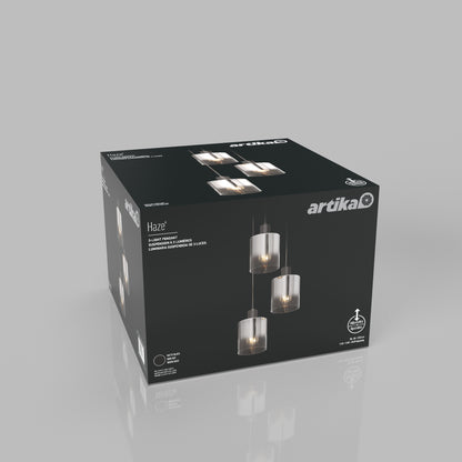 A black Artika box showcases the Haze modern 3-light pendant light glass, featuring three glass shades suspended at varying heights, set against a plain gray background.