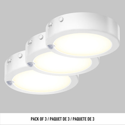 Three round, white Artika Accent under cabinet LED light 3CCT surface-mounted puck lights arranged in a row on a gray background. Text below reads: PACK OF 3 / PAQUET DE 3 / PAQUETE DE 3.