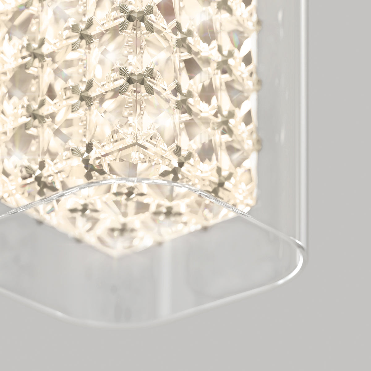 A close-up of the Artika Crystal Cube 1-light LED pendant light, featuring geometric crystal patterns glowing warmly and partially encased in a clear curved glass panel, set against a light gray background.