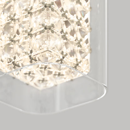 A close-up of the Artika Crystal Cube 1-light LED pendant light, featuring geometric crystal patterns glowing warmly and partially encased in a clear curved glass panel, set against a light gray background.