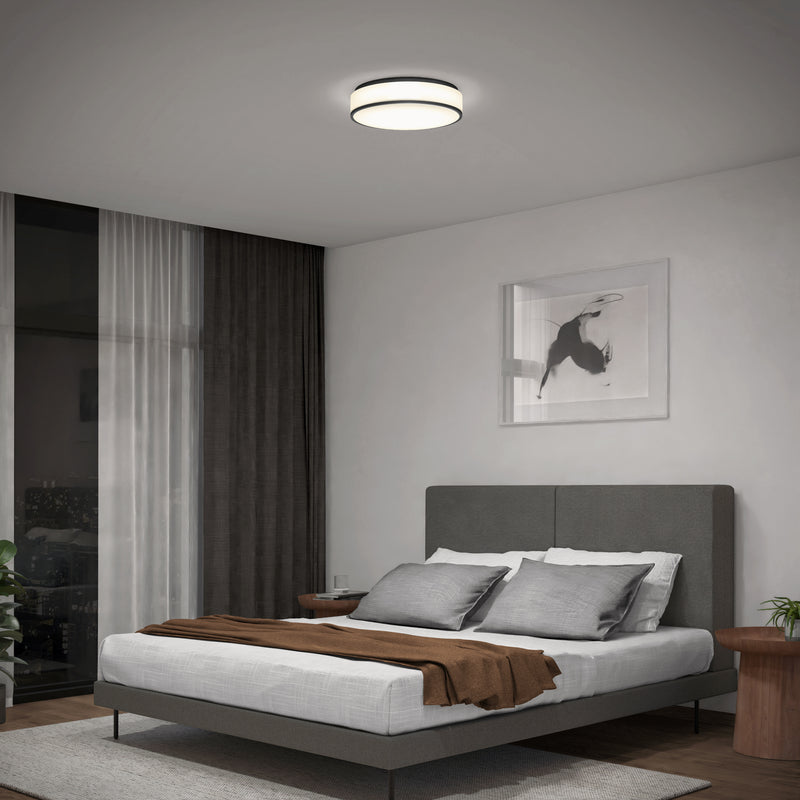A modern bedroom with a grey upholstered bed, white and grey bedding, brown throw blanket, wooden side tables, a large window with curtains, and an Artika Giada 15 in. LED modern flush mount light. A framed photo hangs above the bed.
