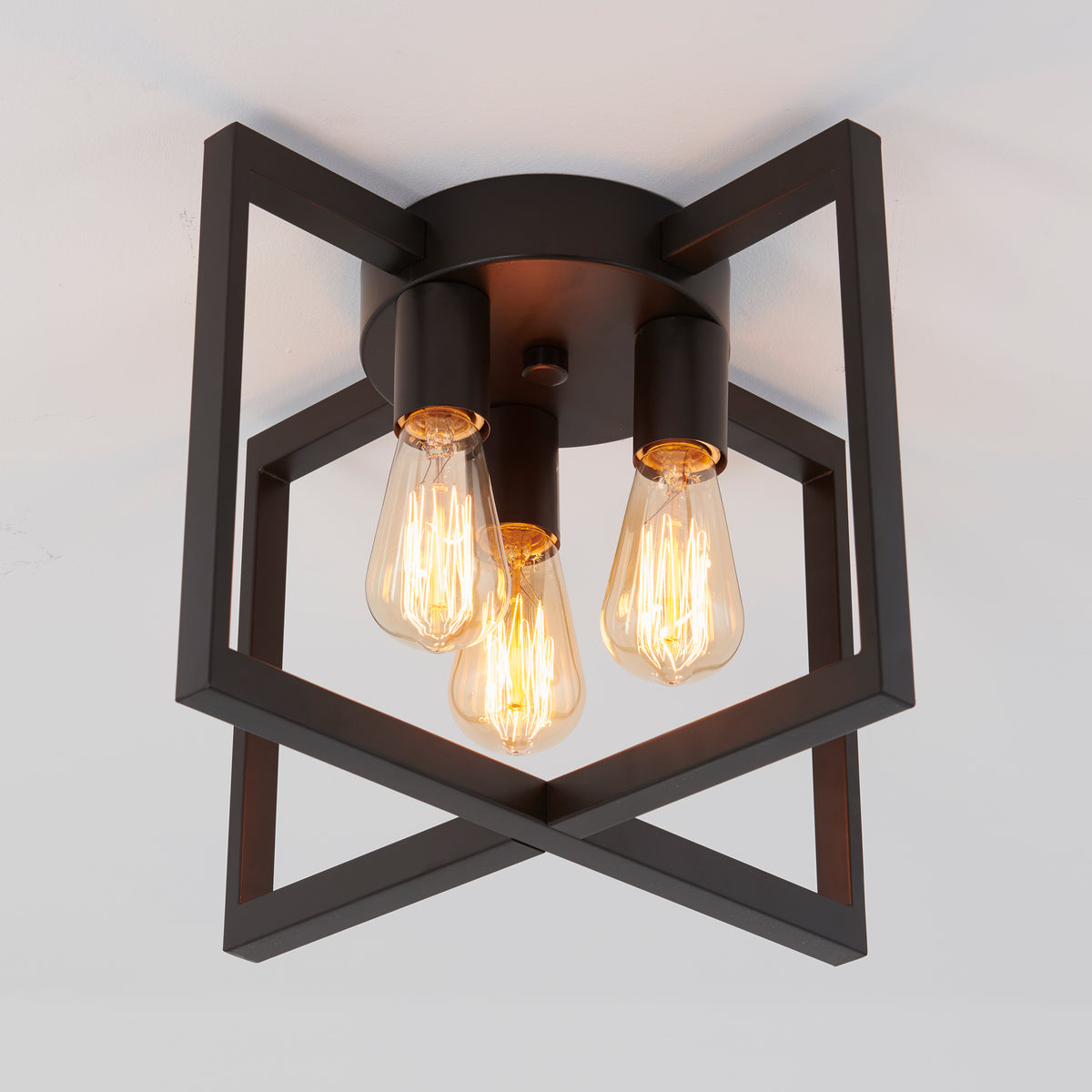 A modern ceiling light fixture with three exposed vintage-style filament bulbs, mounted within a black geometric metal frame against a white ceiling.