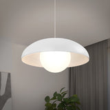 A modern ceiling pendant light with a white, dome-shaped shade and a glowing round bulb hangs in a minimalist room with gray curtains, a plant, and abstract wall art.