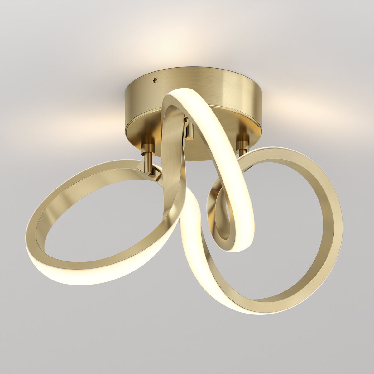 Modern ceiling light fixture with a brushed gold base and three intertwined, glowing LED loops, creating an abstract, sculptural design against a plain white background.