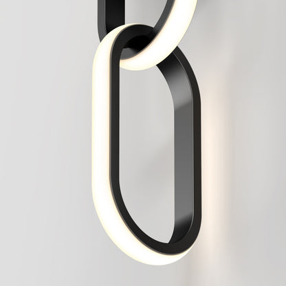 The Artika Catena modern LED wall sconce 5 CCT features a black and white oval design with a glowing edge, inspired by interlocking chain links, and is shown mounted on a plain white wall.