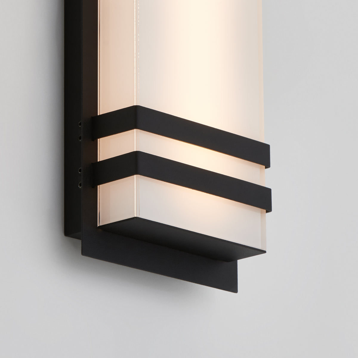 A close-up of the Artika Glowbox 3 indoor-outdoor LED wall light, featuring a frosted glass shade with black metal horizontal bands and a black rectangular backplate, mounted on a light-colored wall.