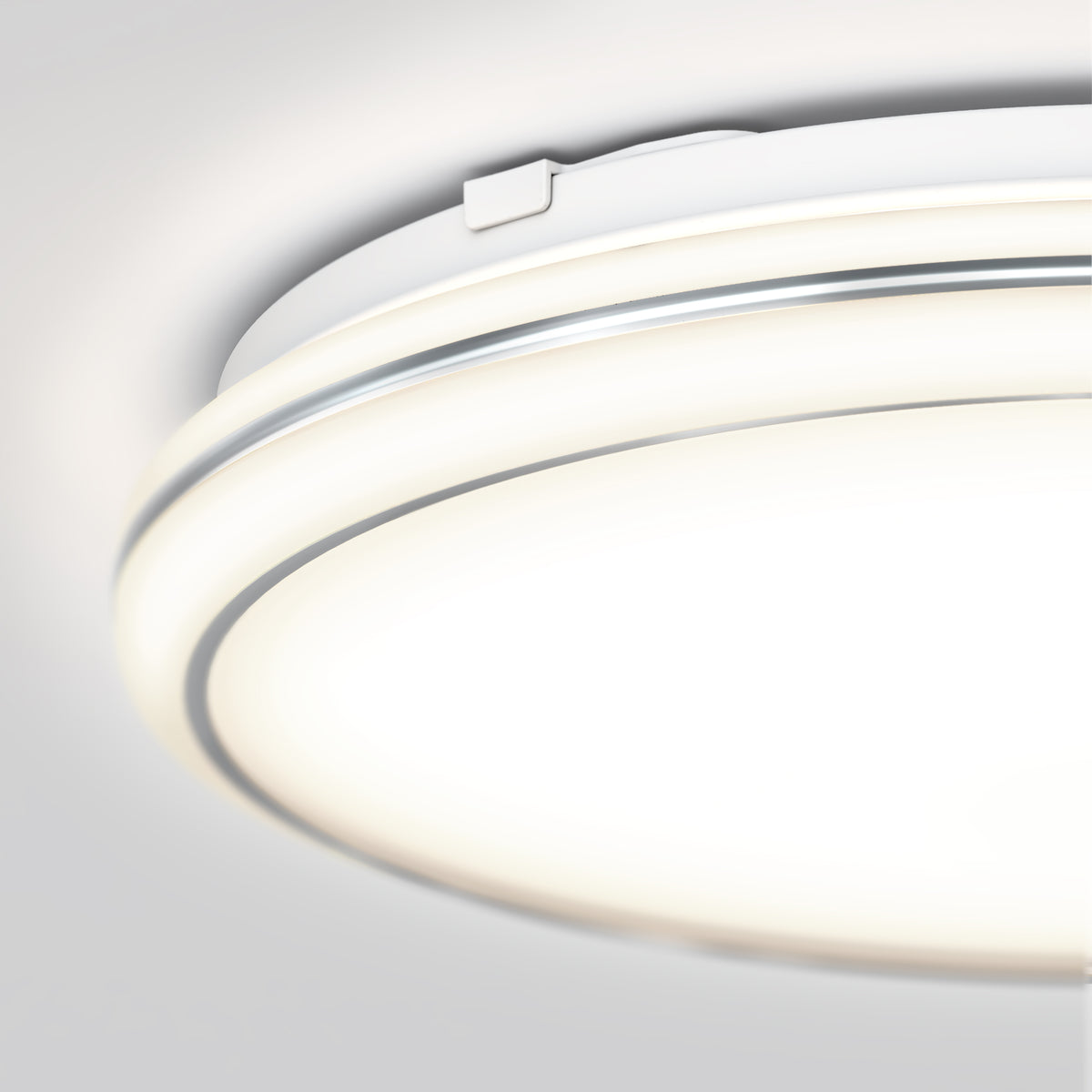 A close-up view of a modern, circular ceiling light fixture with a sleek white and silver design, emitting a soft, bright glow against a light gray ceiling.