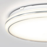 A close-up view of a modern, circular ceiling light fixture with a sleek white and silver design, emitting a soft, bright glow against a light gray ceiling.