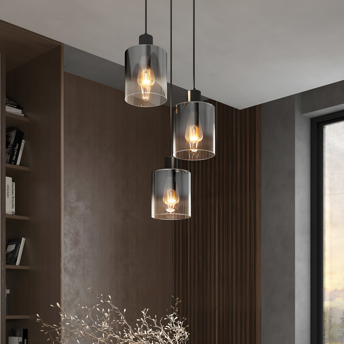 Three modern pendant lights with transparent cylindrical glass shades hang at different heights in a stylish, contemporary room featuring wooden paneling, a bookshelf, and a large window.