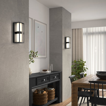 Modern dining area featuring a wooden table, black chairs, and a black sideboard against a gray wall. Two Artika Sherman modern LED indoor-outdoor wall lights (5 CCT) are mounted on the wall, with framed art, plants, and wicker baskets enhancing the decor.