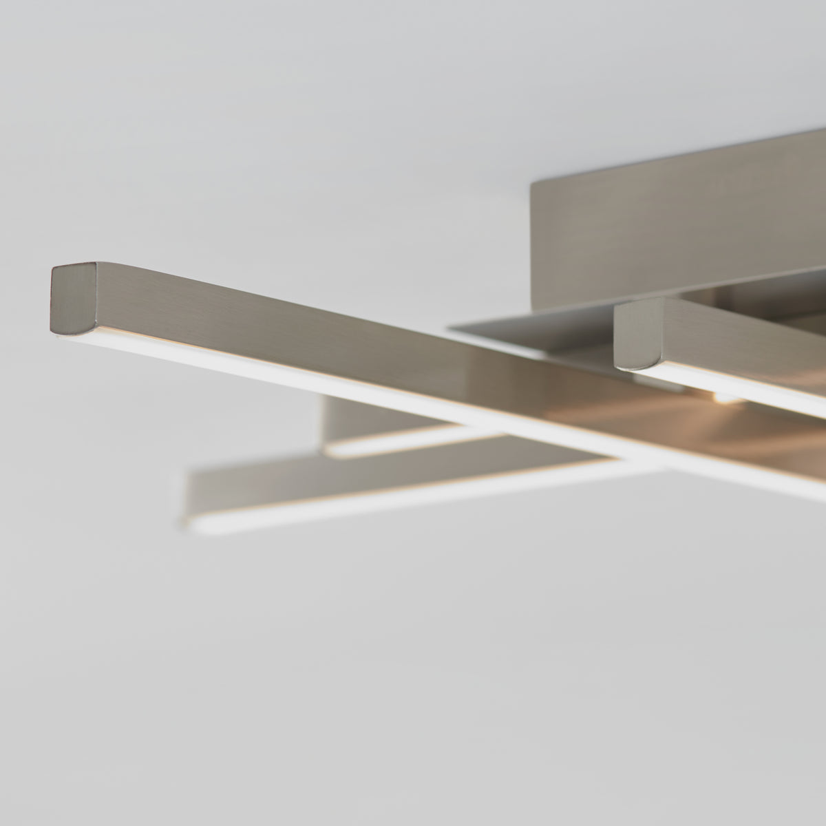 Close-up of a modern ceiling light fixture with three sleek, horizontal metal bars emitting light, set against a plain, light-colored background.