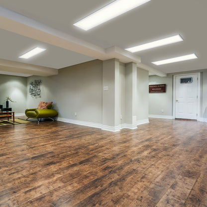 Modern finished basement with wood flooring, beige walls, and Artika Sunray ultra thin LED light panels. Minimalist decor includes a green chair, small table with accents, and a FRIENDS ALWAYS WELCOME sign near the white door.